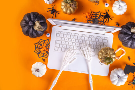 Funny Halloween workplace with laptop flat lay. Office corporation Halloween party invitation, blogger autumn holiday background. White laptop wih Halloween party decor, orange background top view