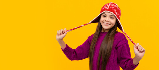 happy child in earflap hat. kid wear warm knitted clothes on yellow background. Banner of christmas child girl, studio kid winter portrait with copy space.
