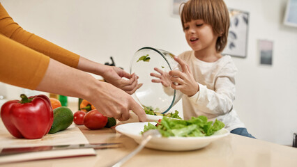 Boy putting on salad from bowl on plate for mother