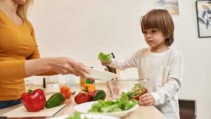 Little boy put on salad on plate in mother hands