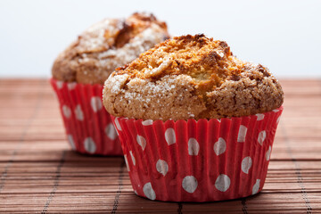 Two muffins in a red bowl over a brown tablecloth