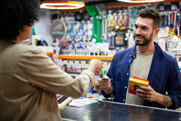 Fototapeta premium Male customer paying with credit card to African American hardware shop worker