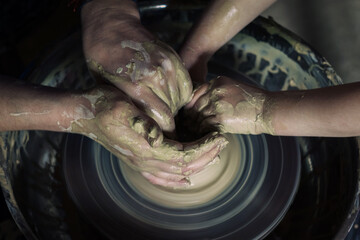 Pottery training. The hands of the female potter guide the movements of the child behind the potter's wheel. View from above