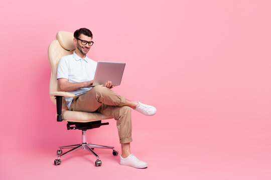 Full length photo of attractive man office worker sit comfort chair use netbook conference empty space isolated on pink color background