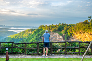Fototapeta na wymiar Asian male tourists looking at the mountain view and fog in the morning at canyon Nam Nao in Phetchabun Province, unseen Thailand.