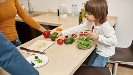 Obraz na płótnie Canvas Boy putting avocado and mixing salad near parents
