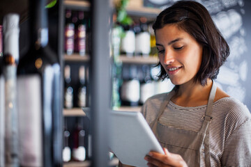 Wine store worker taking inventory of bottles on digital tablet