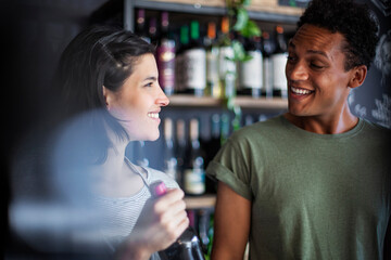 Female liquor store worker holding bottle while talking with customer