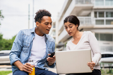 Mid-shot of African-American man and Latin American woman using laptop while working outdoors