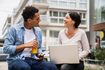 Mid-shot of diverse couple of co-workers discussing business matters while working outdoors