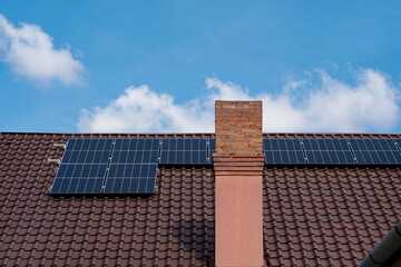 Solar panels mounted on the rooftop of a residential house. Sunny blue sky, brick chimney, no people