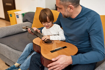 Father teach son play notes on acoustic guitar