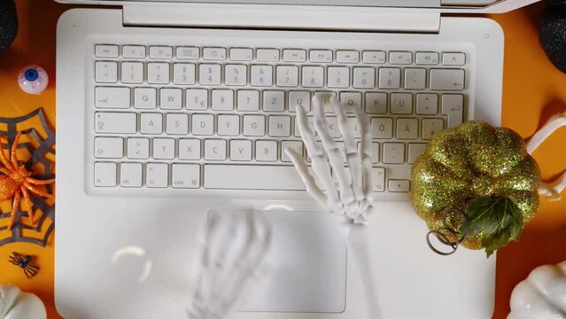 Funny Halloween workplace with laptop. Office corporation Halloween party invitation, blogger autumn holiday background. Decorative skeleton hands tapping on laptop buttons and touchpad, typing text
