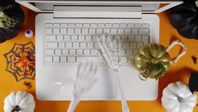 Funny Halloween workplace with laptop. Office corporation Halloween party invitation, blogger autumn holiday background. Decorative skeleton hands tapping on laptop buttons and touchpad, typing text