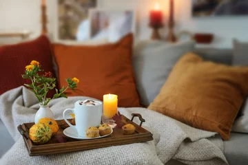 Fototapeten Relaxation with hot chocolate on a tray with candles and autumn decoration on the couch in a cozy living room, copy space, selected focus © Maren Winter