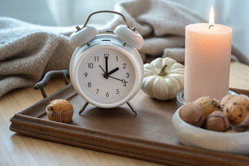 White vintage alarm clock, candle, autumn decoration and sweets on a nightstand with a natural...
