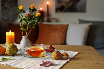 Tea time in autumn, glass cup, biscuits, pumpkins and candle on a table in a cozy home, copy space,...
