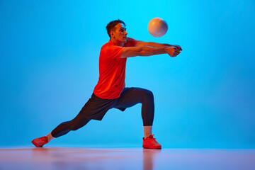 Receiving ball. Volleyball player training with ball isolated on blue studio background in neon...