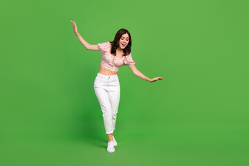 Full size photo of nice cheerful woman with curly hairdo wear white trousers top look down isolated on green color background