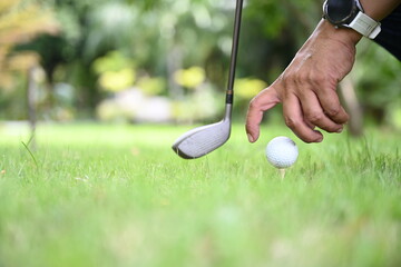 Man golfer hand holding golf ball on golf tee with club or putter placed on the side on a blurred golf course background. Man wearing watch organizing child Golf before hitting

