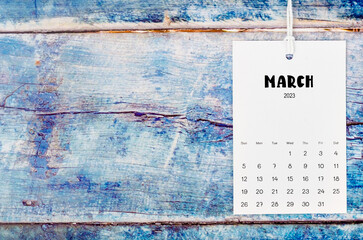 The March 2023 calendar page hanged with white rope  on old blue wooden background.