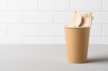Eco friendly wooden cutlery in craft paper cup on the brick wall background. Recycling eco concept. Space for text