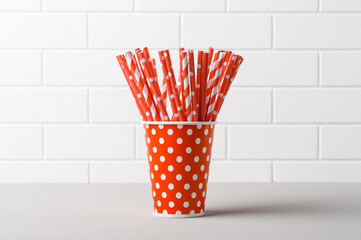 Pile of red striped straws in paper cup for birthday party. Brick wall. Pop Art style.