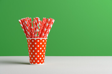 Pile of red straws in paper cup for birthday party. Bright green wall. Pop Art style. Space for text