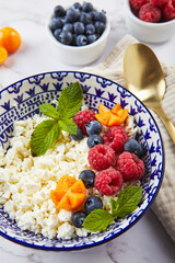 Cottage cheese in bowl garnished with raspberries, blueberries, physalis and mint leaves on white background