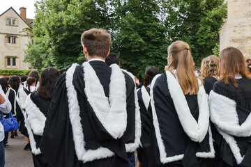 back view of Male and female fresh graduate students with gown and academic address walk in campus...