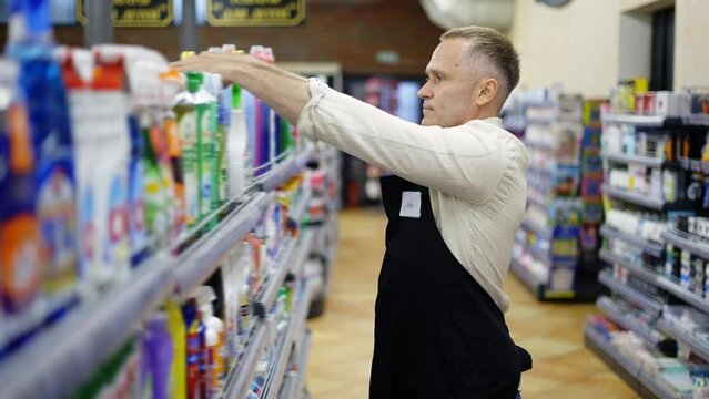 A middle-aged store worker arranges goods on a shelf. Work in the store. Control the product. Happiness