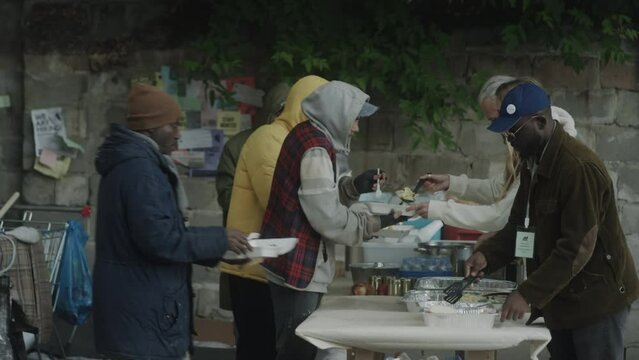 Wide shot of volunteers serving free meals for homeless at soup kitchen on street