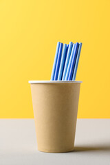 Pile of blue straws in craft paper cup for birthday party. Bright yellow wall. Pop Art style. Recycling eco concept.
