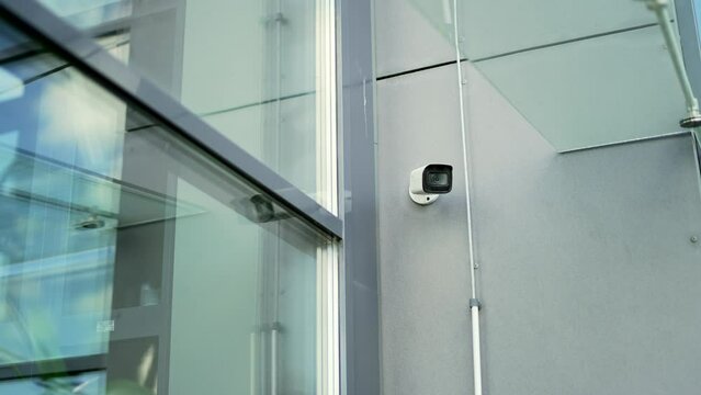 White CCTV security surveillance camera built into the metal wall of the modern glass office building outside. installed outdoor in city. Privacy, urban, protection, house system control, secure video
