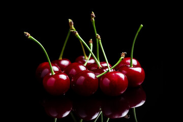 Red cherry berries on a black background with mirror. Three cherries