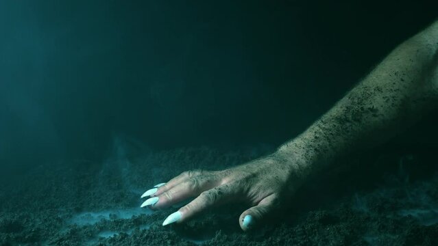 A terrible hand with claws emerges from the fumes of smoke and scratches the graveyard soil.