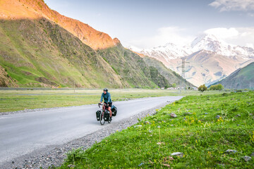Caucasian male cyclist bicycle touring in caucasus KAzbegi mountains and Kazbek peak in the background. Travel around caucasus. Cycle around the world