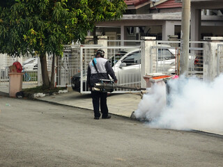 MELAKA, MALAYSIA - JUNE 1, 2022: The fogging of mosquito repellent is being carried out using a special machine. Spray workers need to wear a special face mask to avoid smelling the poison.