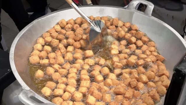 slow motion of chef is frying tofu in a large skillet.