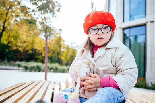 Happy family moments in the city. Photo portrait of little girl wearing red beret and coat sits at bench at city street outdoors.