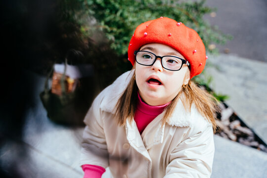 Cute inquisitive little girl in eyeglasses with special needs looking at mother. Portrait of beautiful little girl in red beret