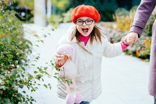 Happy laughing little girl in eyeglasses with special needs holding mother's hand on a walk in autumn time outdoor.