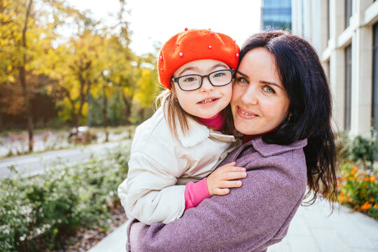 Happy family moments concept. Portrait of cute curious little daughter in eyeglasses wearing red beret and mother hugging outdoor in the city street. Happy family moments concept.