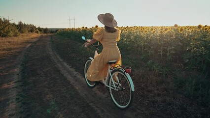 Rural woman in timeless dress riding retro styled white bicycle on country road alone near sunflowers field. Vintage fashion, amazing adventure, countryside activity, healthy lifestyle.