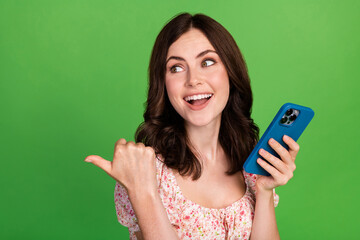 Photo of funny impressed girl dressed print blouse messaging modern gadget pointing empty space isolated green color background
