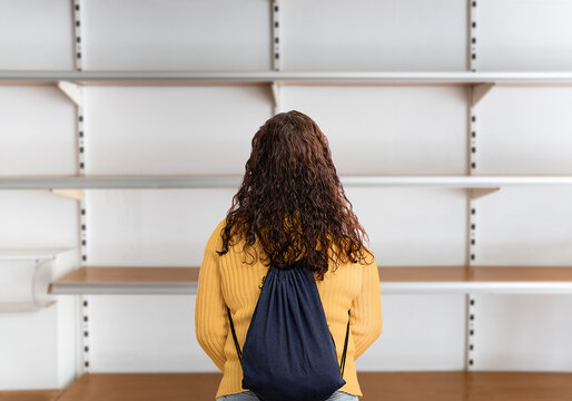 Rear view of young woman standing in front of empty shelf in a supermarket