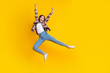 Fototapeta na wymiar Full length photo of shiny lucky girl dressed plaid shirt jumping high rising fists isolated yellow color background
