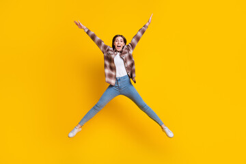 Fototapeta na wymiar Full length photo of excited pretty girl dressed plaid shirt jumping high like star isolated yellow color background