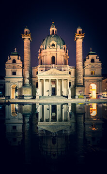 Vertical image of Karslkirche church building and its reflections at night time with tourists sitting nearby. Tourism and historical buildings in Viena, Austria