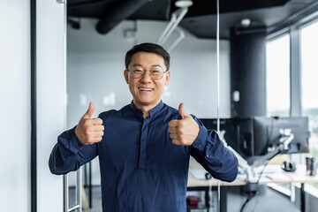 Fototapeta na wymiar Portrait of successful asian businessman, man working in modern office looking at camera and smiling, broker trader showing thumbs up.